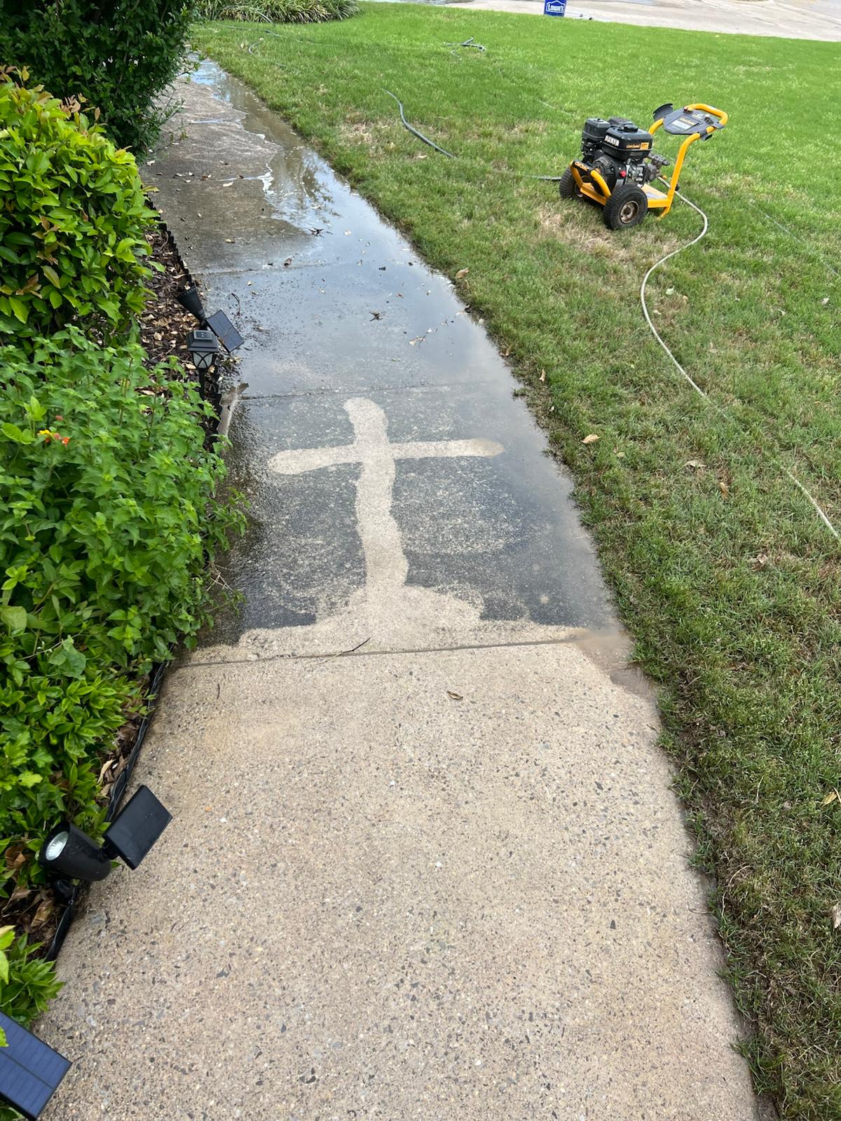 A clean cross washed into a dirty sidewalk, mid-job